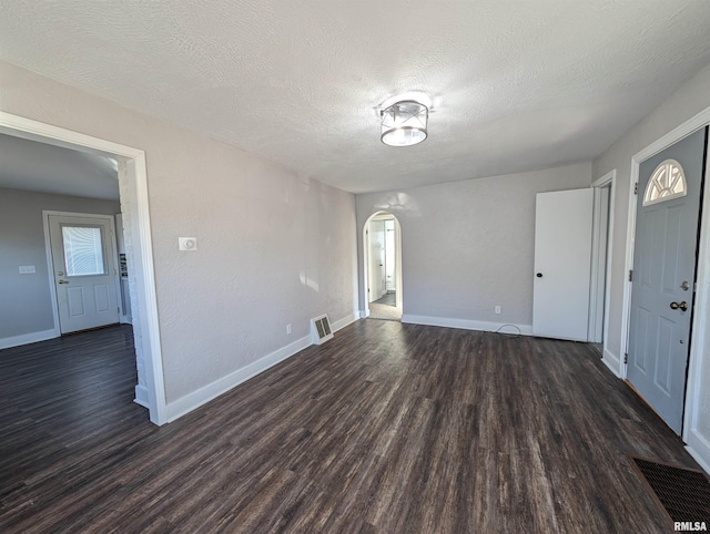 unfurnished room with visible vents, arched walkways, and dark wood-style flooring