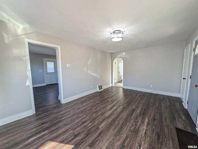 unfurnished room with dark wood-type flooring, arched walkways, visible vents, and a textured ceiling