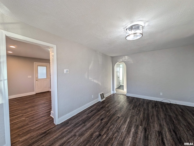 spare room featuring dark wood-type flooring, arched walkways, a textured ceiling, and baseboards