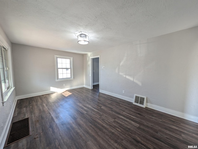 spare room with dark wood-style floors, visible vents, and baseboards