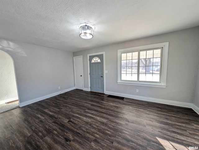 entryway with visible vents, a textured wall, dark wood-type flooring, a textured ceiling, and baseboards