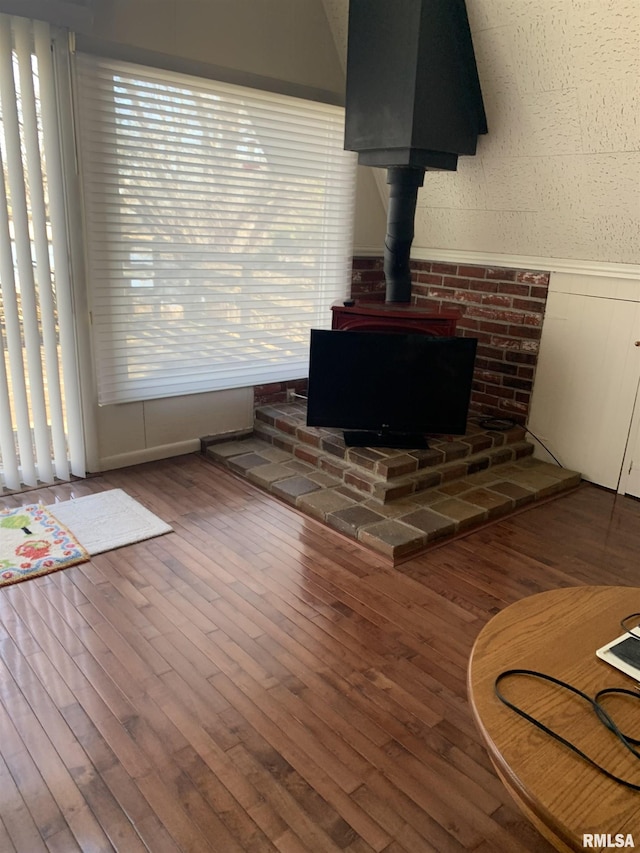 living area with wainscoting, wood finished floors, and a wood stove