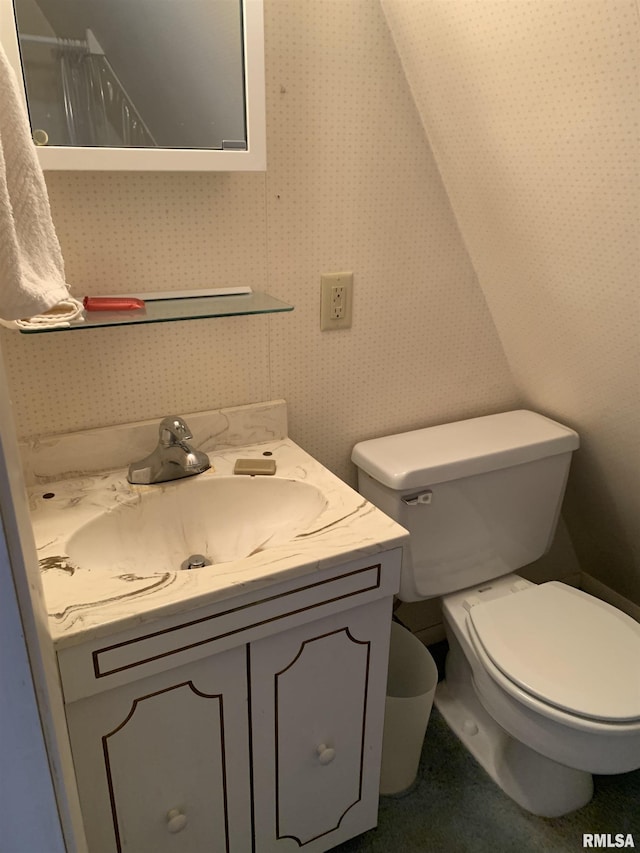 bathroom with toilet, vanity, and wallpapered walls