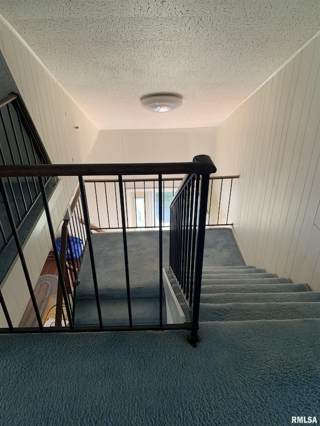 stairway featuring carpet floors, vaulted ceiling, and a textured ceiling