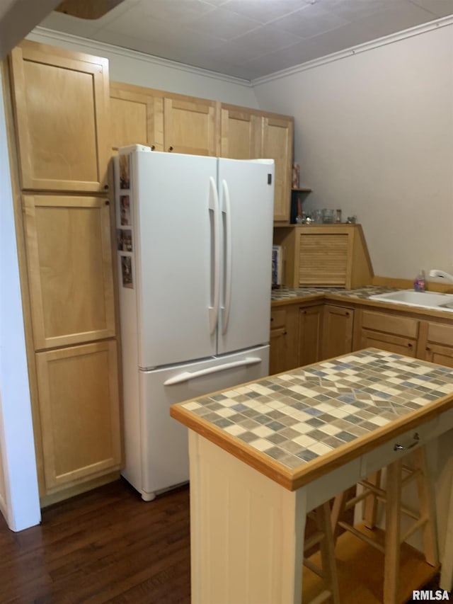 kitchen featuring tile counters, light brown cabinetry, a sink, and freestanding refrigerator