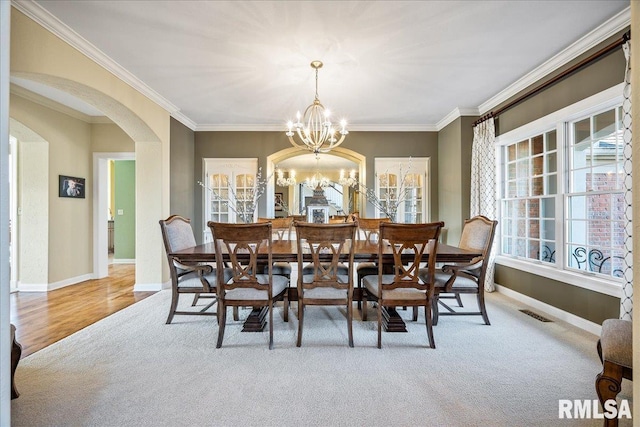 dining space with arched walkways, crown molding, a chandelier, and baseboards