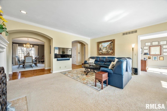 carpeted living room featuring baseboards, visible vents, arched walkways, and crown molding