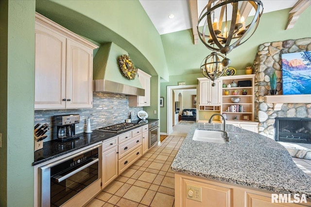 kitchen featuring decorative backsplash, wall chimney exhaust hood, an inviting chandelier, stainless steel appliances, and a sink