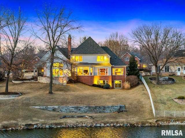 back of house with a water view, a chimney, fence, and brick siding