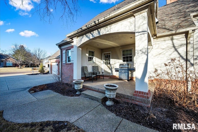 entrance to property with a garage, driveway, stucco siding, a patio area, and brick siding