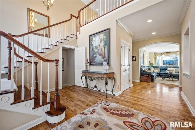 foyer featuring arched walkways, ornamental molding, wood finished floors, and a towering ceiling