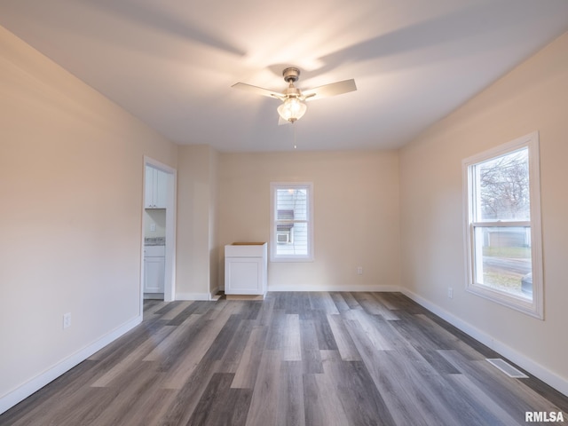 spare room featuring ceiling fan, baseboards, dark wood-type flooring, and a wealth of natural light