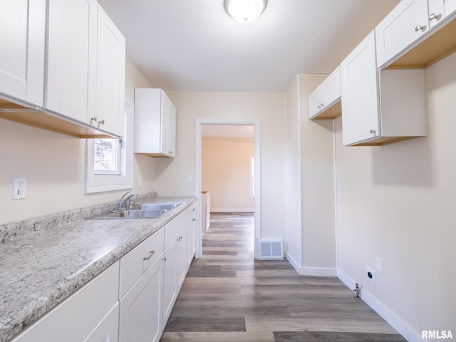 kitchen featuring baseboards, visible vents, white cabinets, wood finished floors, and a sink