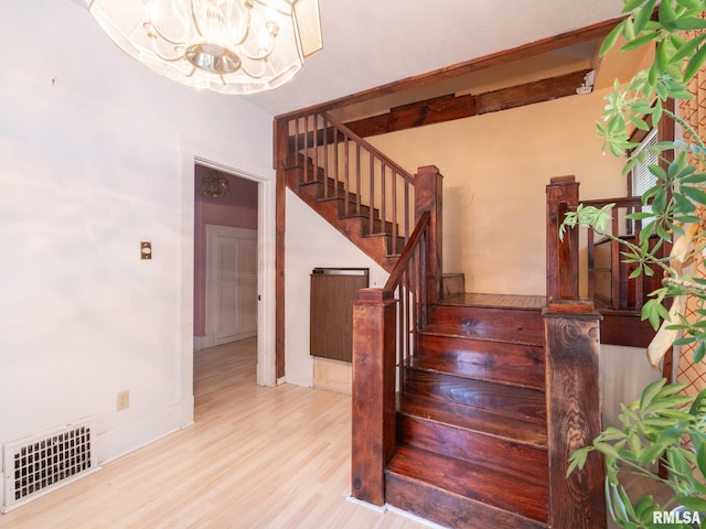 stairway featuring visible vents, a notable chandelier, baseboards, and wood finished floors