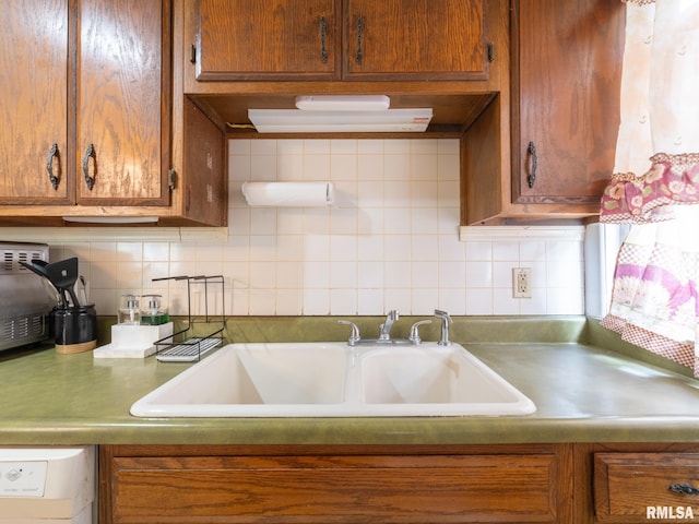 kitchen featuring brown cabinetry, white dishwasher, a sink, and decorative backsplash