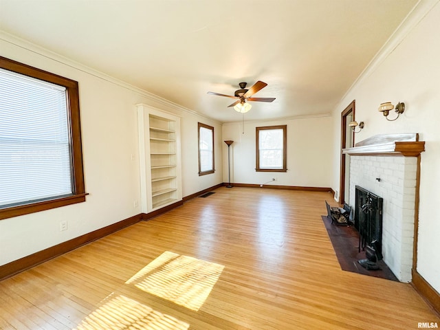 unfurnished living room with ornamental molding, a brick fireplace, light wood-style flooring, and baseboards