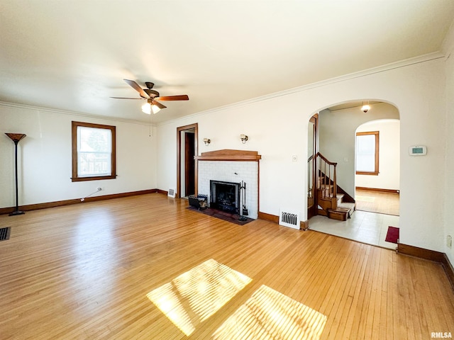 unfurnished living room featuring arched walkways, a fireplace, visible vents, ornamental molding, and light wood-type flooring