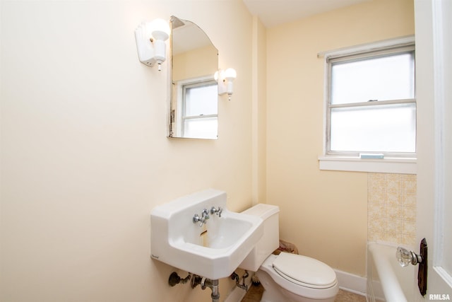 full bath featuring toilet, a sink, a washtub, and baseboards