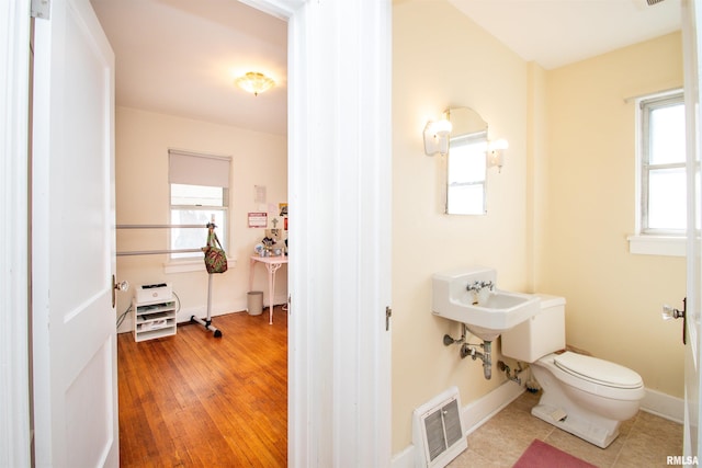 half bathroom featuring toilet, baseboards, visible vents, and a healthy amount of sunlight