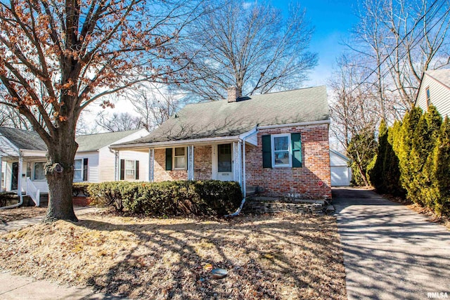 view of front of home featuring roof with shingles, brick siding, a chimney, and an outdoor structure