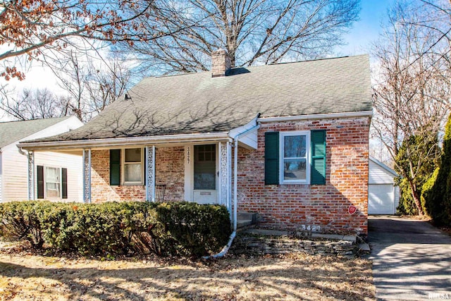 view of front of house with brick siding, roof with shingles, a chimney, and an outbuilding