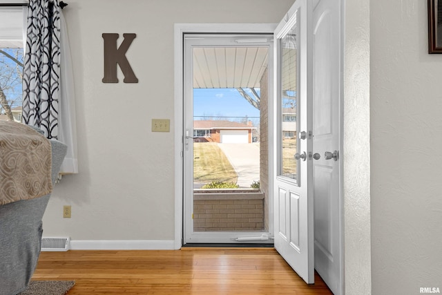 foyer entrance featuring visible vents, a textured wall, baseboards, and wood finished floors