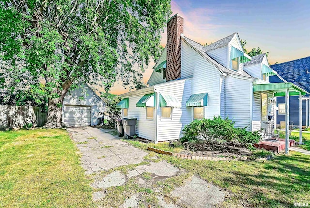 view of front of home featuring a garage, a chimney, a lawn, and an outdoor structure