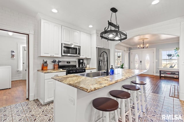 kitchen with arched walkways, ornamental molding, appliances with stainless steel finishes, white cabinetry, and a kitchen breakfast bar