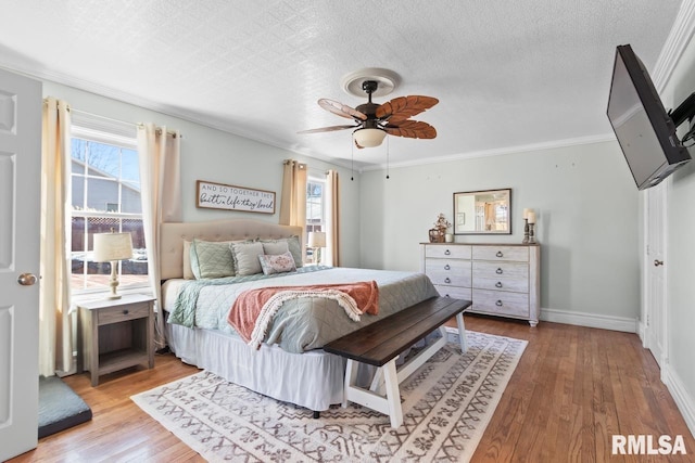 bedroom featuring a ceiling fan, wood finished floors, baseboards, a textured ceiling, and crown molding