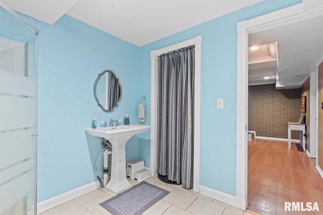 full bath featuring tile patterned floors, brick wall, and baseboards