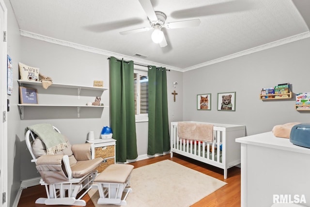 bedroom featuring wood finished floors, visible vents, ceiling fan, a crib, and ornamental molding