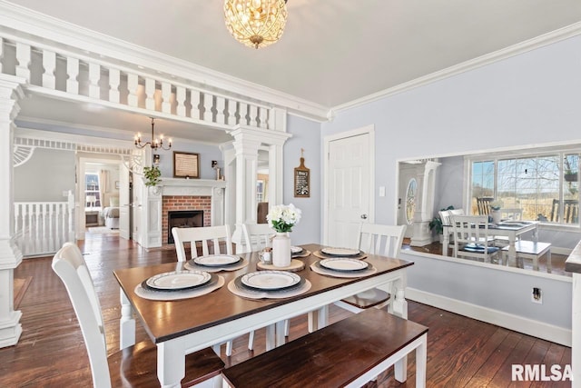 dining area with ornate columns, an inviting chandelier, a brick fireplace, and wood-type flooring