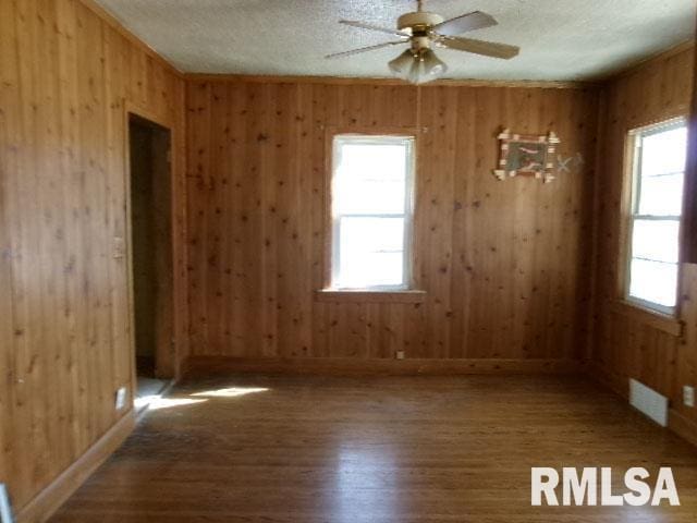 spare room with visible vents, a ceiling fan, wood finished floors, a textured ceiling, and wood walls