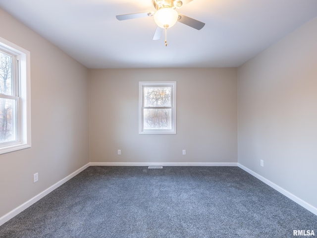 spare room with a ceiling fan, dark colored carpet, and baseboards