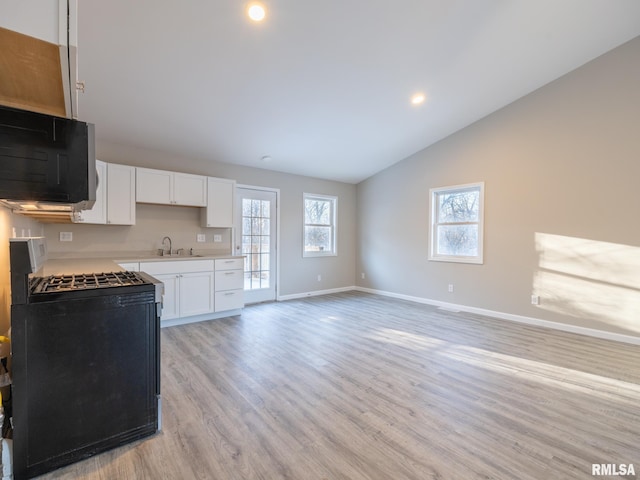 kitchen with light countertops, light wood-type flooring, black appliances, white cabinetry, and a sink