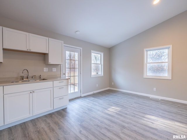 kitchen featuring light wood finished floors, lofted ceiling, light countertops, white cabinets, and a sink