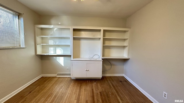 unfurnished office featuring a baseboard radiator, built in study area, dark wood finished floors, and baseboards