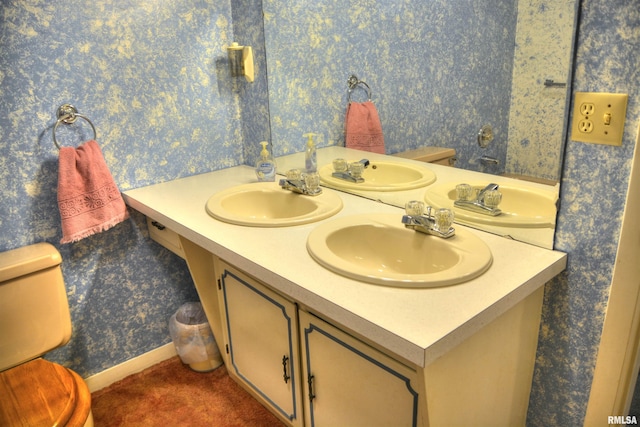 bathroom with double vanity, a sink, toilet, and wallpapered walls