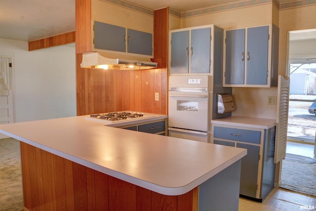 kitchen featuring white appliances, wallpapered walls, blue cabinets, light countertops, and under cabinet range hood