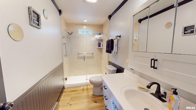 bathroom with toilet, wainscoting, vanity, a shower stall, and wood finished floors