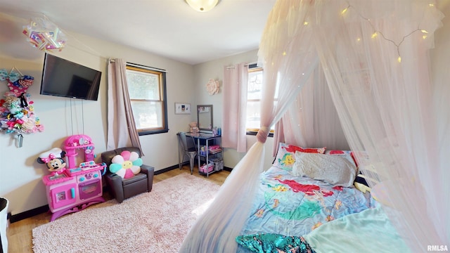 bedroom with multiple windows, wood finished floors, and baseboards