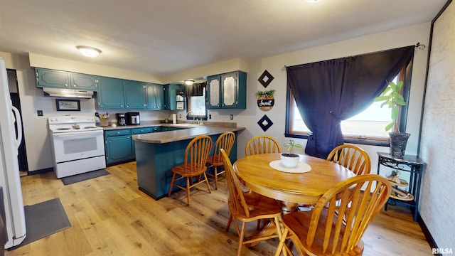 kitchen featuring white appliances, light wood finished floors, a peninsula, under cabinet range hood, and a sink