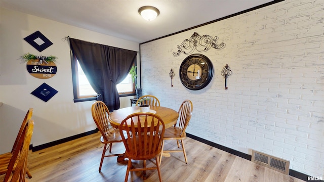 dining space featuring light wood finished floors, baseboards, brick wall, and visible vents