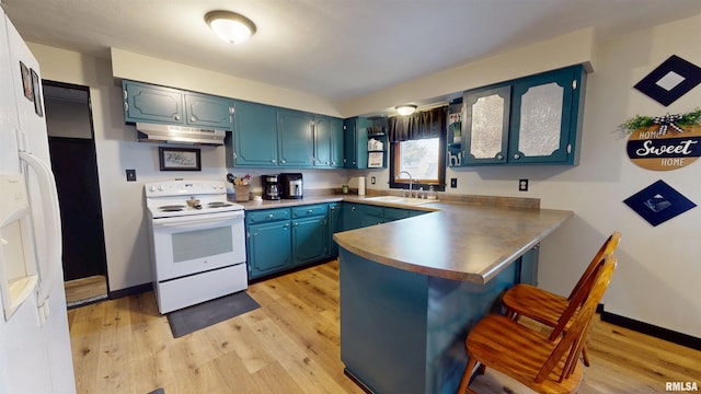 kitchen featuring a breakfast bar area, a sink, a peninsula, white appliances, and under cabinet range hood