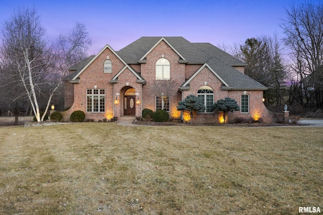 traditional-style house featuring brick siding, a lawn, and a shingled roof