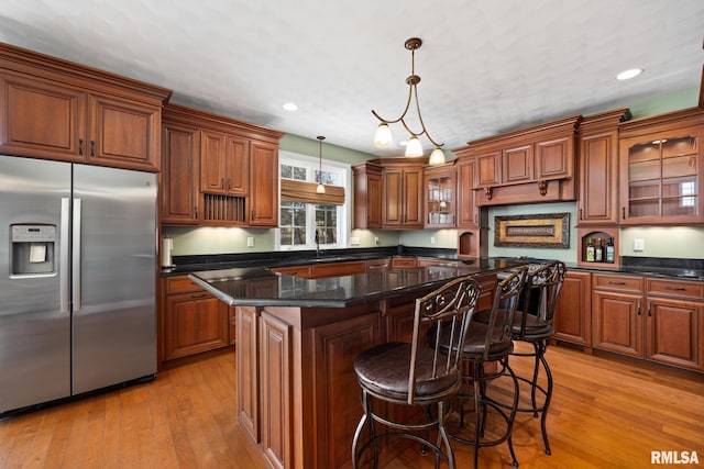 kitchen with a sink, light wood-style floors, stainless steel refrigerator with ice dispenser, brown cabinets, and decorative light fixtures