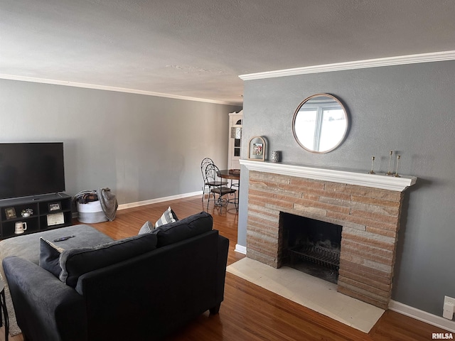 living area with a fireplace, crown molding, a textured ceiling, wood finished floors, and baseboards