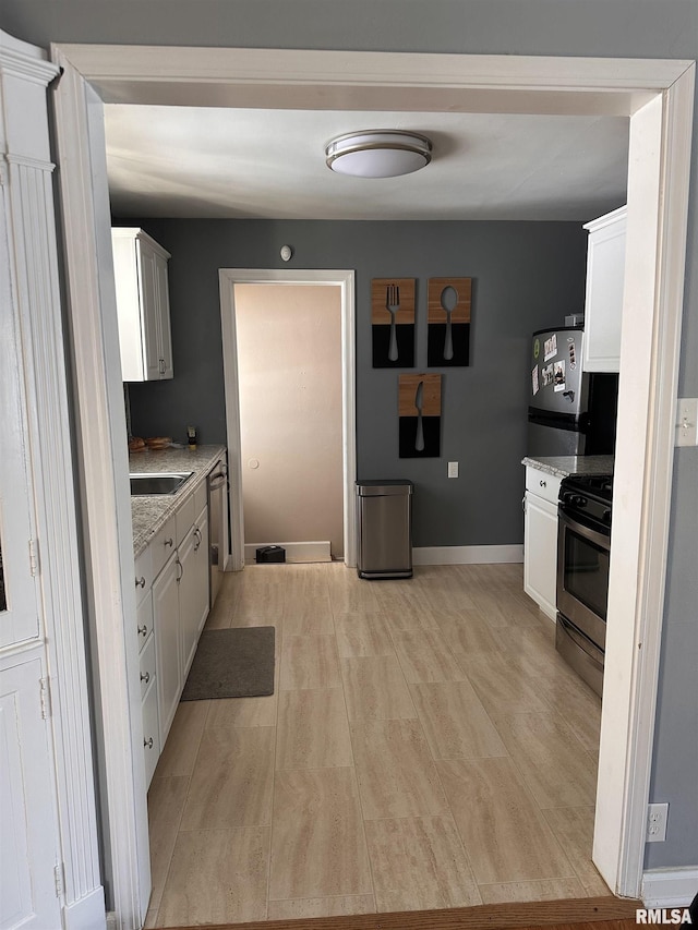 kitchen featuring baseboards, stainless steel appliances, a sink, and white cabinets