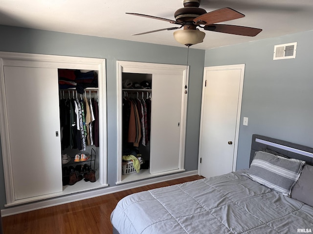 bedroom featuring ceiling fan, visible vents, two closets, and wood finished floors