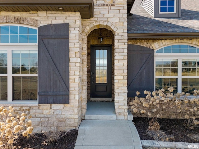 entrance to property featuring stone siding and a shingled roof